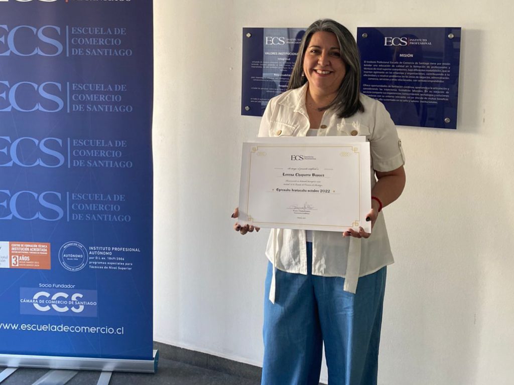Smiling woman holding a framed certificate at a blue ECS banner backdrop showing 'Escuela de Comercio de Santiago' logos? and text on the certificate visible in the frame, indoors.