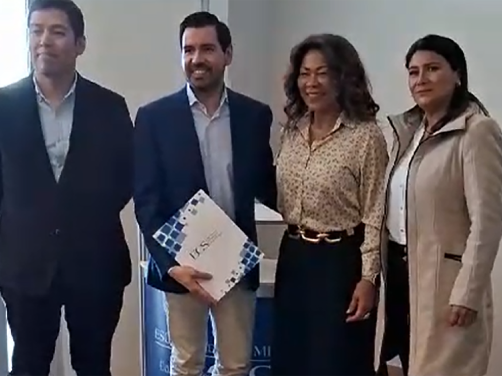 Four professionals posing for a group photo indoors, two men in suits and two women in smart attire, one man holding a white brochure or booklet with blue accents.