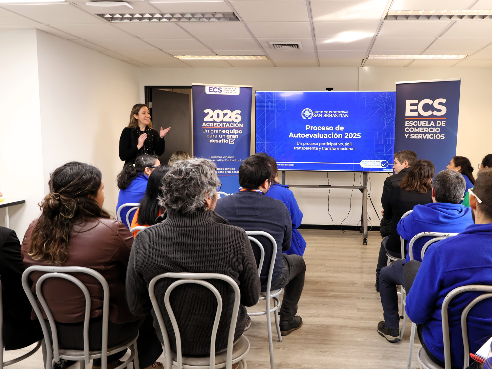 Instructor presenting to a seated audience in a classroom with ECS banners and a screen about Autoevaluación 2025.