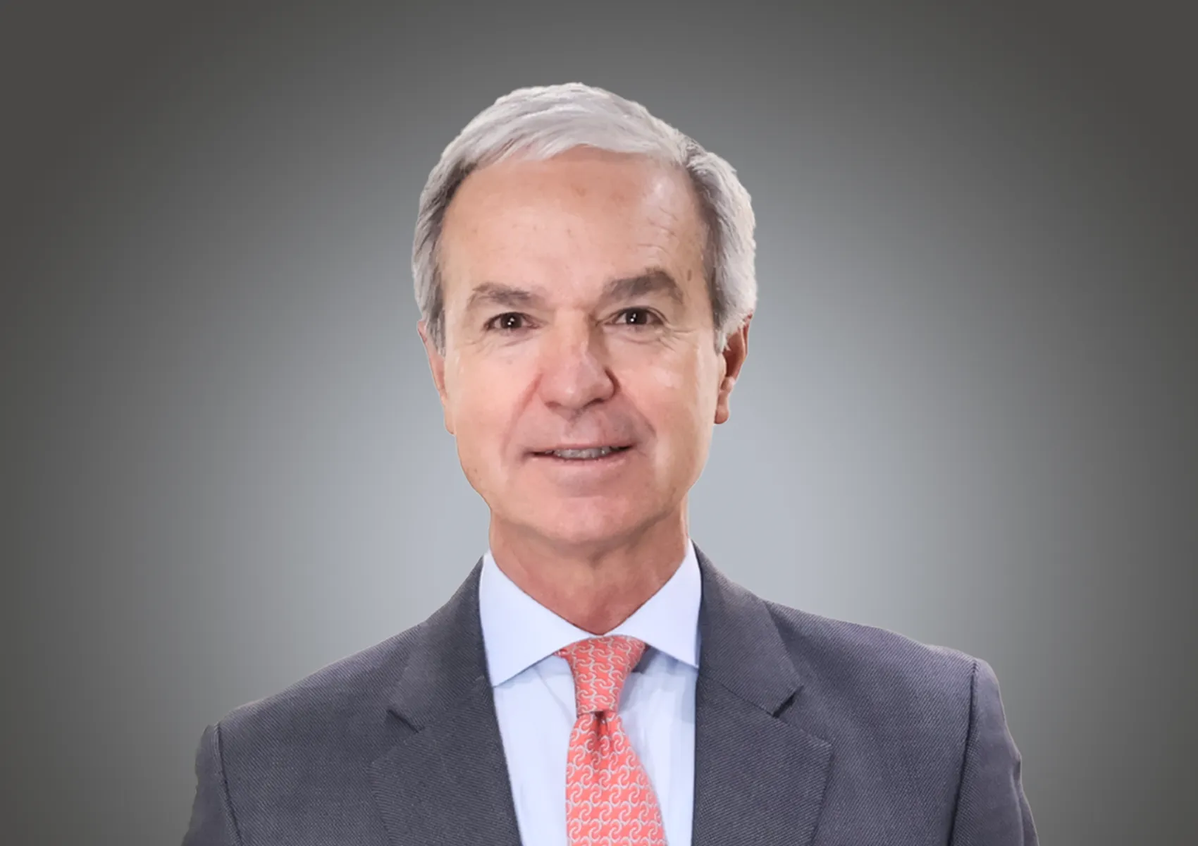 Portrait of a middle-aged man in a gray suit and coral tie, against a gray gradient background. (head-and-shoulders)​