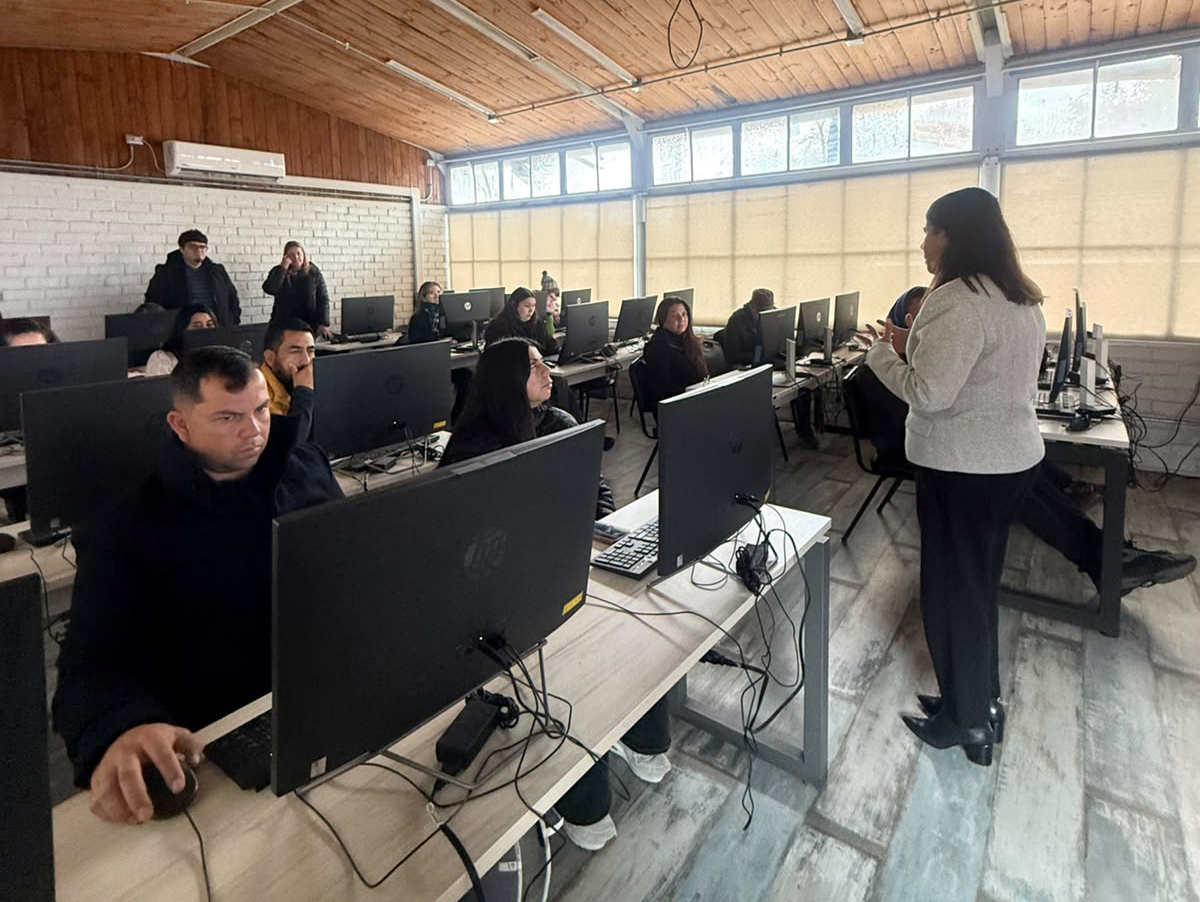 Instructor stands at the front of a computer lab addressing adults seated at desks with HP monitors and keyboards.