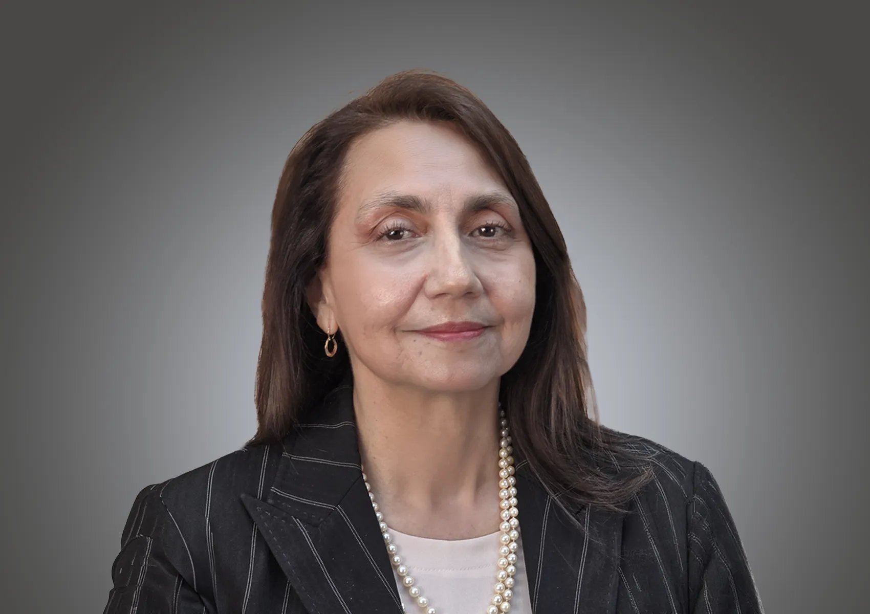 Portrait of a smiling woman with brown hair in a pinstripe blazer and pearl necklace against a gray gradient backdrop.